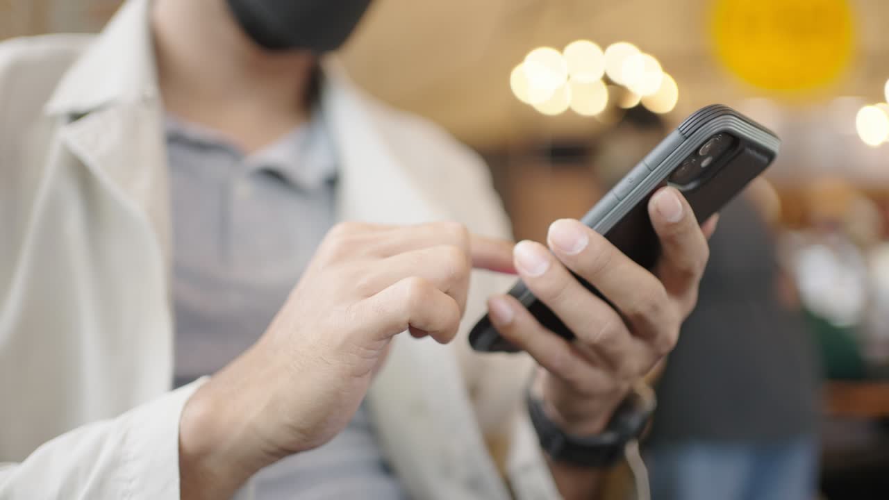 un joven empresario con una máscara quirúrgica está tomando una videoconferencia con los clientes a través de un teléfono inteligente conectado a internet.