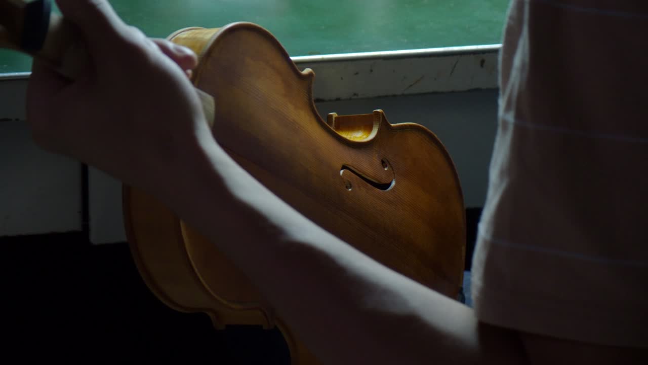 Le fasce di violino ricevono un'attenta applicazione di vernice da un liutaio esperto, valorizzando la fiammatura dell'acero e il tono ambra caldo all'interno di un ambiente di laboratorio, primo piano statico
