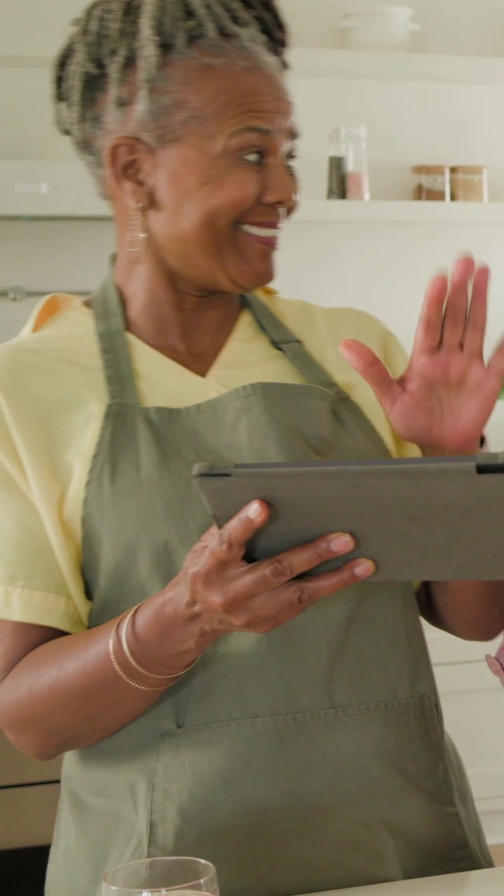 Vertical video: Hearing voice cook in green apron at counter chopping taking tablet checking recipe