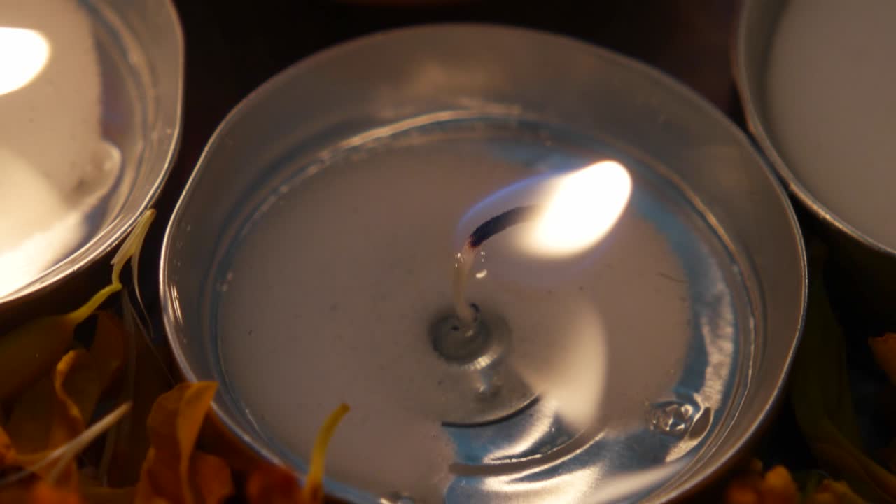 Inclinación a primer plano extremo de Diyas o lámpara de barro india en un plato de plata con pétalos de caléndula, encendidas para Diwali 'Festival de la luz', rodeadas de velas de té encendidas.