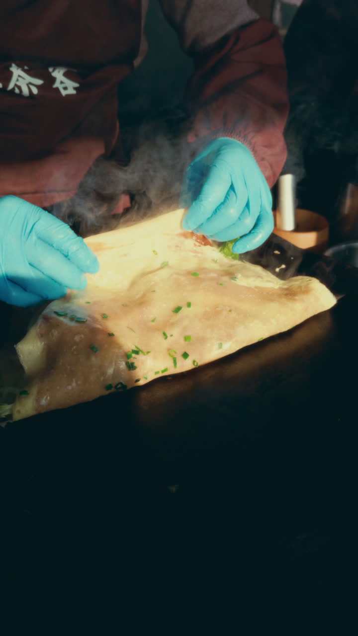 Steam rises as hands in blue gloves fold a flatbread with green toppings in Wuzhen