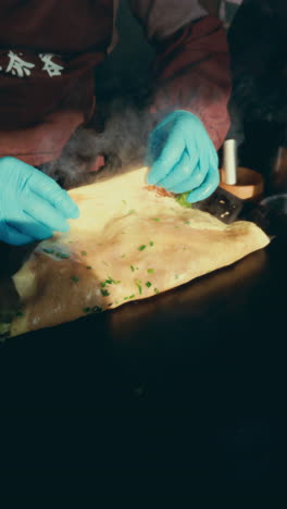 steam rises as hands in blue gloves fold a flatbread with green toppings in wuzhen