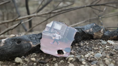 close up gimbal shot of burnt photo of child on ground leaning against burnt log