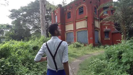 Stylish-alone-young-male-walk-towards-creepy-abandoned-house-in-forest