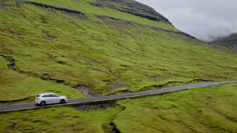 a car drives through a lush green valley in the faroe islands on a cloudy day