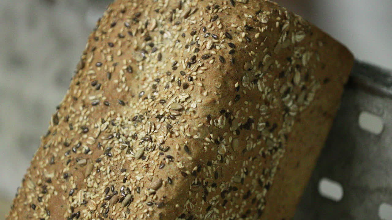 Close up View Of A Brown Loaf Bread With Sesame Seeds Rest On A Baking Tray In The Bakery. - Pan Down, slow motion