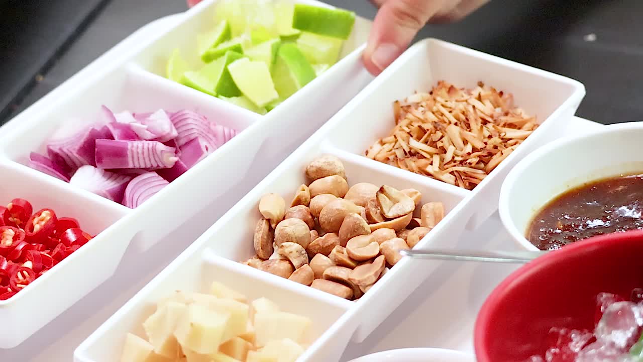 Close-up of vibrant ingredients arranged in trays for preparing Thai leaf wraps, showcasing peanuts, onions, and sauce.