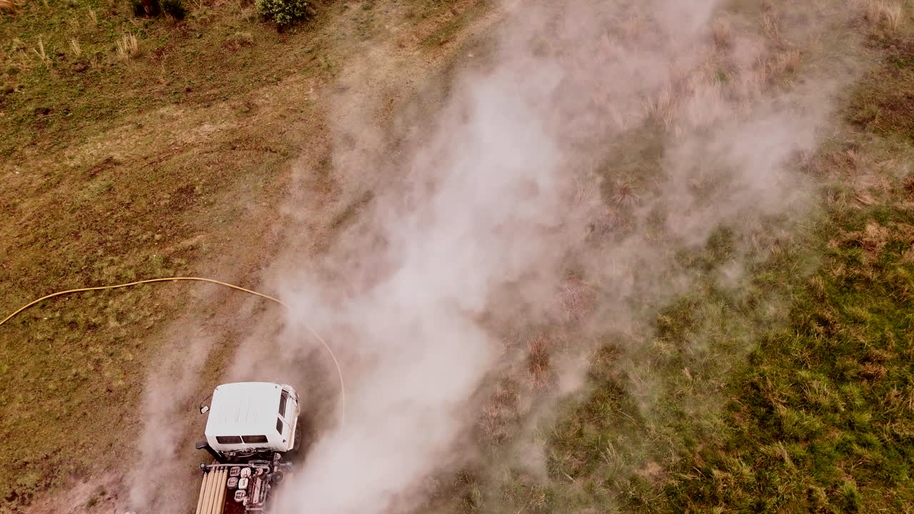 un disparo de drone inverso captura una plataforma de perforación en medio de un campo cubierto de hierba, el humo se eleva