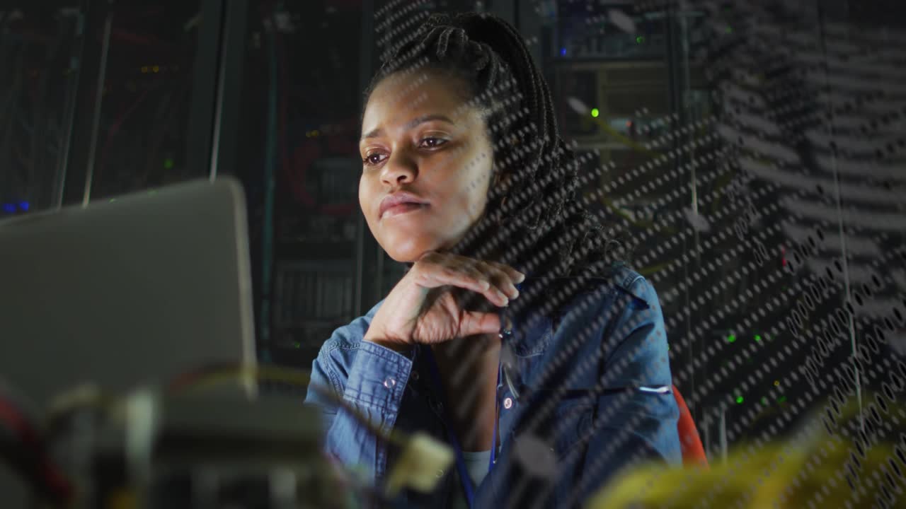 Vertical video: Gazing tech monitoring laptop at server racks, shifting grill casting dot overlay