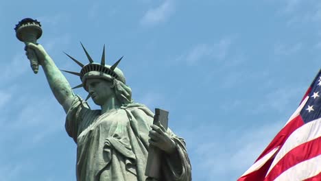 the camera pansleft across a rippling american flag revealing the statue of liberty in the background