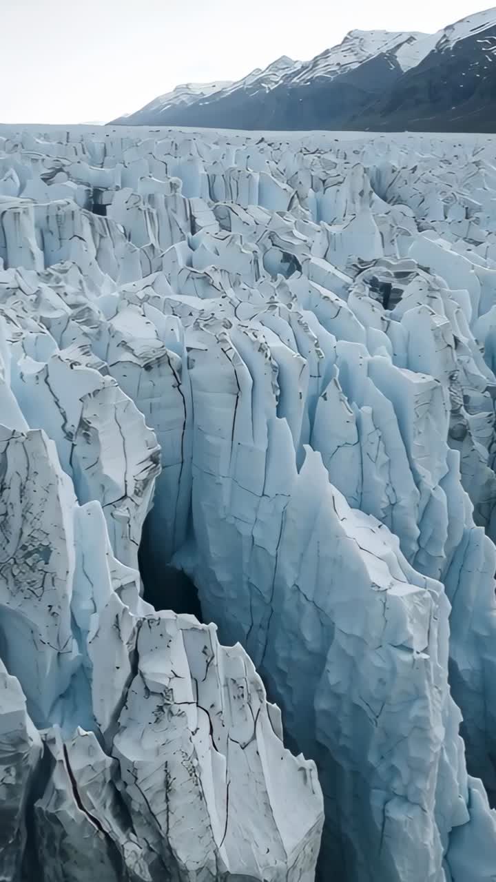 Video verticale: drone che si allontana durante la scansione di un ghiacciaio in una valle, mostrando crepacci e detriti fino alle cime