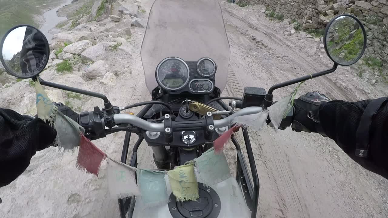 Riding a motorbike over rock earth with prayer flags on the handle bars and leather gloves to hold on with