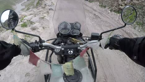 riding a motorbike over rock earth with prayer flags on the handle bars and leather gloves to hold on with