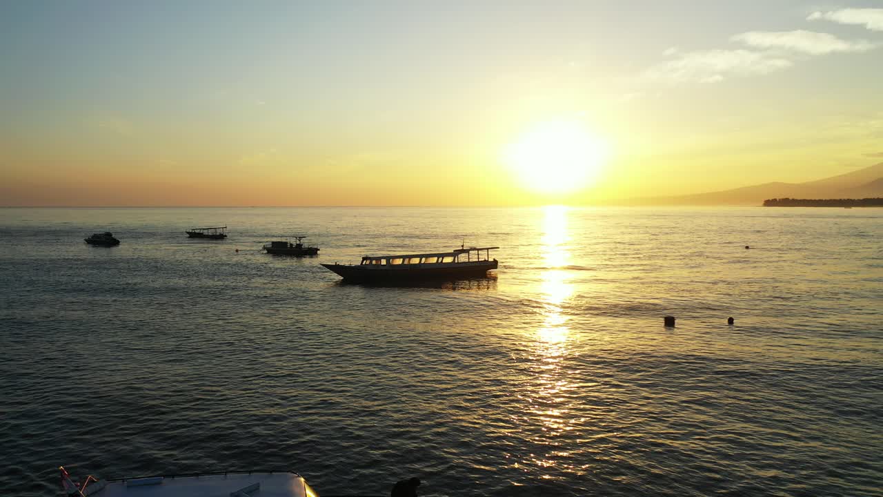 Silhouette of anchored boats on vibrant water of lagoon reflecting bright sky with yellow sun at sunset in Malaysia
