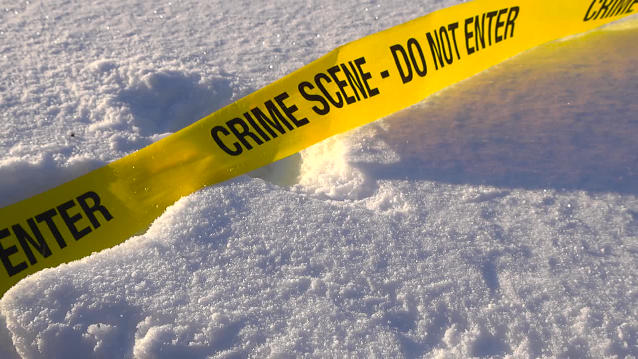Forensic poilice science yellow colroed crime scene tape ribbon abandoned on a white fluffy snow covered area during winter sunny day with sun creating shadows on the snow, video gliding over it
