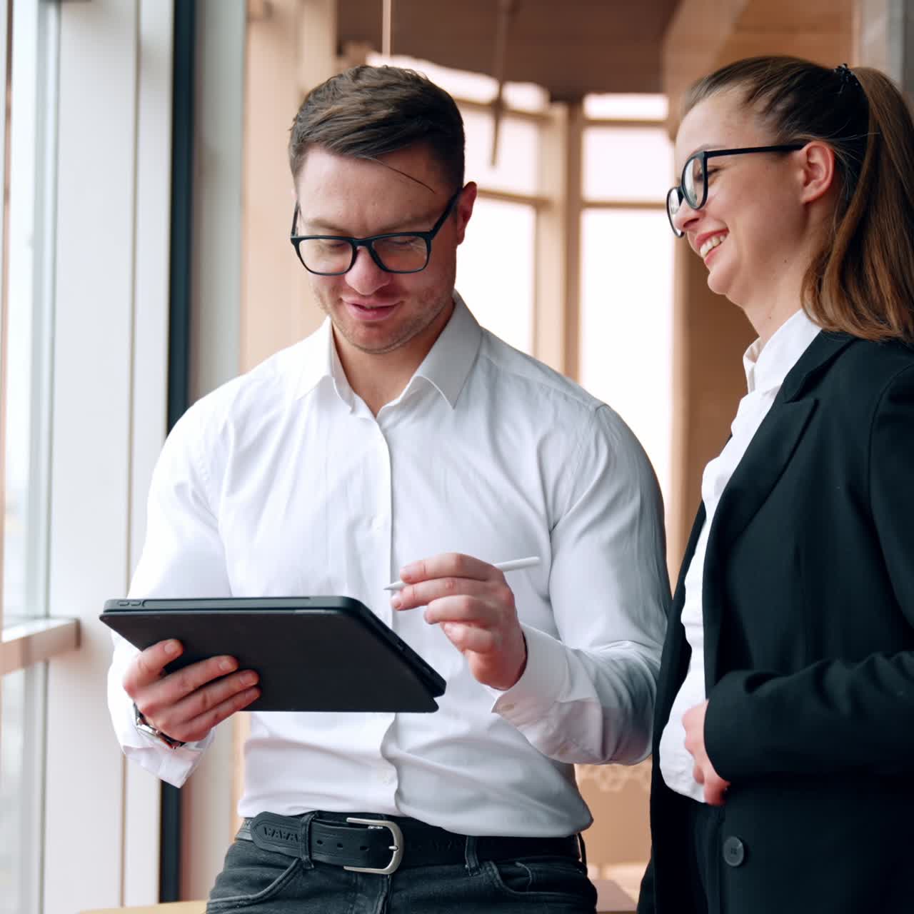 Colegas positivos se comunicam no trabalho. Um homem usa um I-pad e uma mulher ao lado conversa com ele