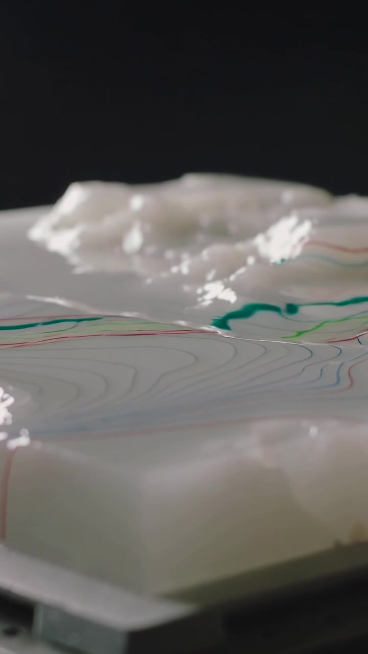 Video verticale: Gel bianco fluido che si sposta, con inchiostri che si muovono lungo un vassoio su una rastrelliera.