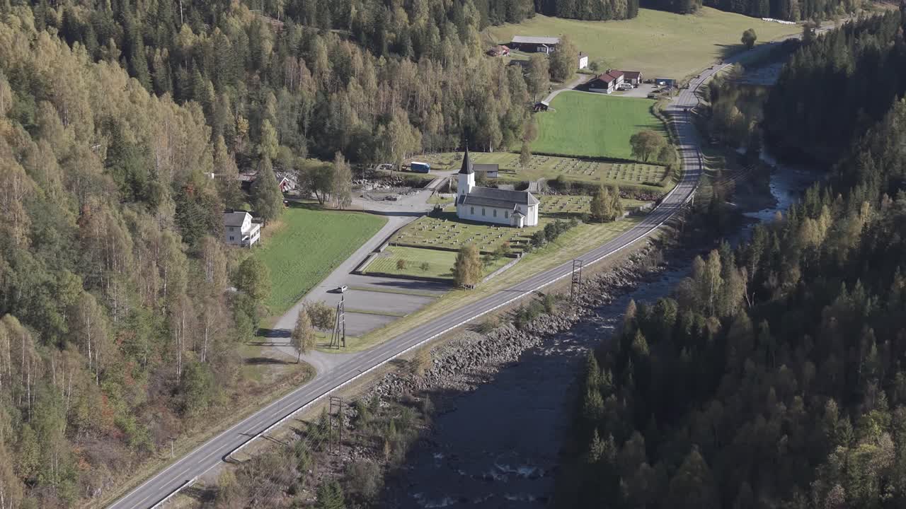 A white church and graveyard in the middle of beautiful valley in Uvdal, Norway. Zooming out drone footage