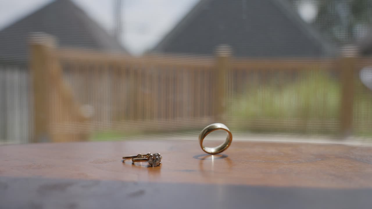 Shiny golden wedding ring spinning on round wooden table reflecting in window glass