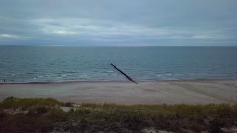 Establishing-aerial-view-of-Baltic-sea-coast-on-a-overcast-day,-old-wooden-pier,-white-sand-beach,-low-waves-crushing-against-the-coast,-climate-changes,-wide-angle-drone-shot-moving-forward