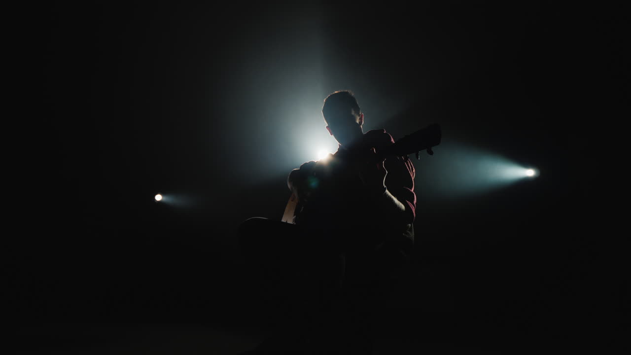 En ung mand spiller guitar og sidder på scene 5