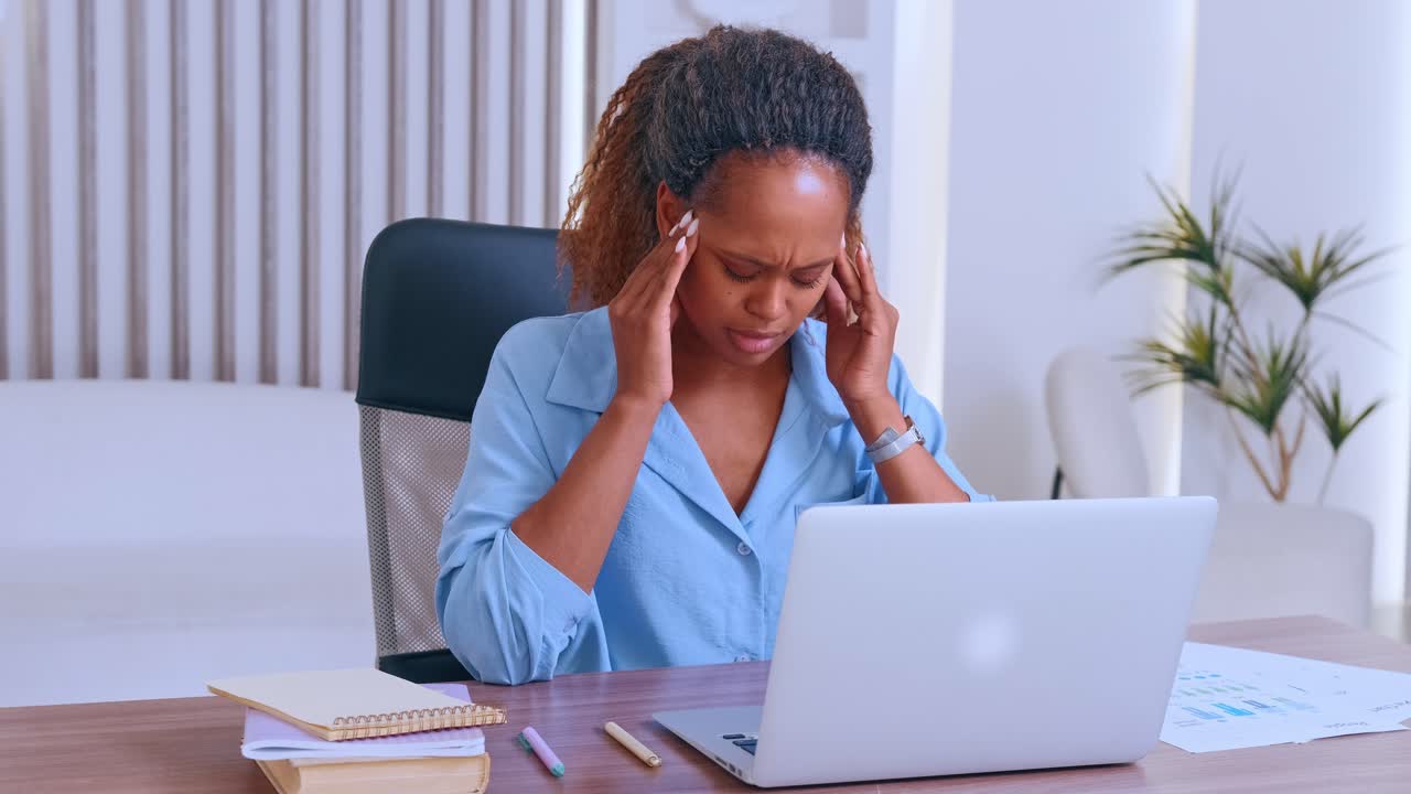 Young tired african american woman working with laptop clutching head