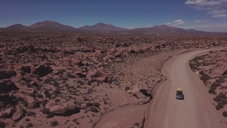 vista aérea de un 4x4 en una polvorienta carretera roja en la reserva nacional de vida silvestre andina eduardo avaroa, levantando lentamente la vista para abrirse al valle de las rocas, "valle de rocas" en uyuni, bolivia