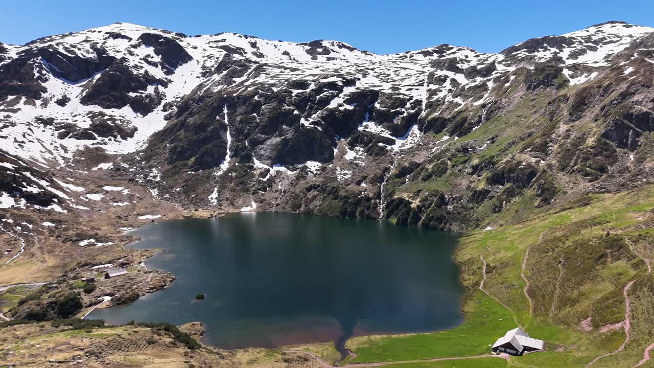 Alpine lake Murgsee in Switzerland framed by rugged mountain peaks with snow patches and green slopes, reflecting the clear sky and tranquil landscape in a serene natural mountain setting