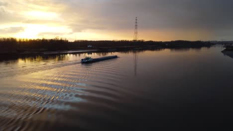 cargo barge boat sailing in river scheldt during golden sunset, aerial ascend shot