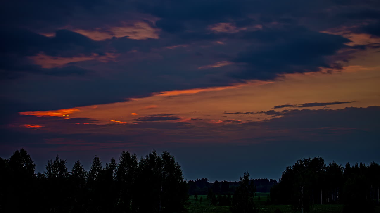Static shot of dark clouds passing by in timelapse over green forest along the grasslands in timelapse during evening time