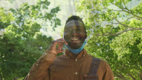 camino del bosque en contra con el hombre afroamericano bajó la máscara de la cara hablando en el teléfono inteligente mientras caminaba