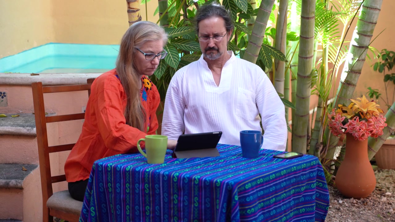 Mature woman looking at a tablet computer is joined by a mature man.