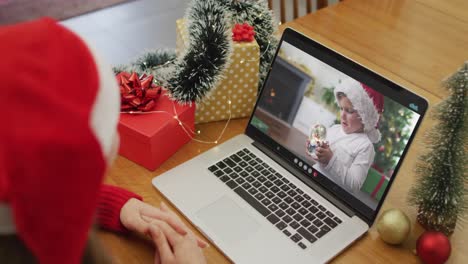 Caucasian-senior-man-having-christmas-video-call-on-laptop-with-grandson-on-screen