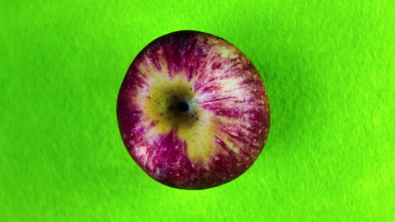 Rotating apple on bright green background, showcasing its texture and color contrast