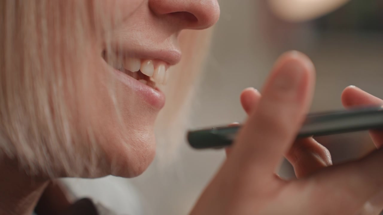 Nahaufnahme einer lächelnden weißen Frau, die ins Telefon spricht, spielerische Sprachnachricht für den Liebhaber, leichtes Lachen, Kopfhörer, Aufnahme einer Melodie-Idee, Lofi-Heimstudio-Vibe, lässiger Songwriter-Moment, Fingertippen, weicher Fokus.
