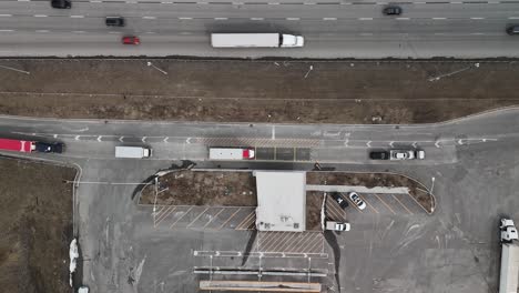 Toma-Aérea-De-Un-Lapso-De-Tiempo-Apuntando-Directamente-Hacia-Abajo-A-Una-Estación-De-Pesaje-Junto-A-Una-Carretera-Muy-Transitada-Donde-Llegan-Camiones-Y-Vehículos-Comerciales-Para-Su-Inspección.