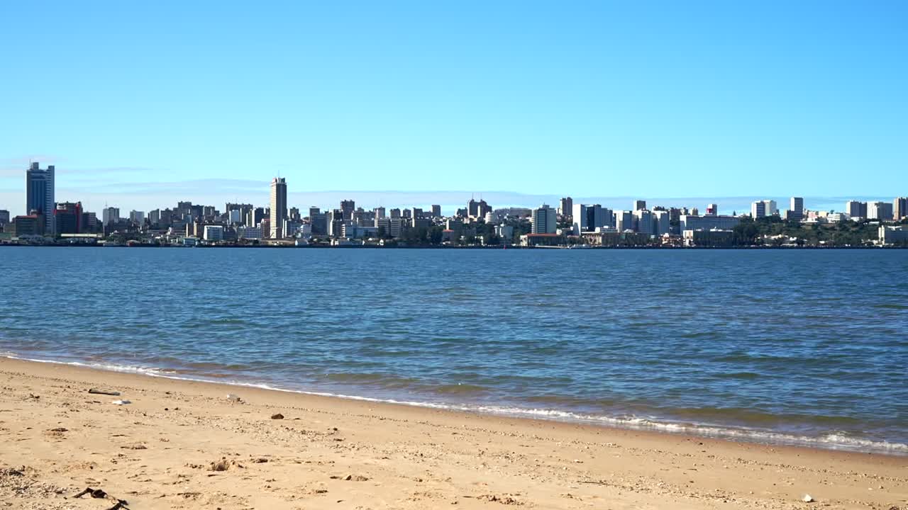 Pemandangan cakrawala panorama Maputo, Mozambik melintasi Teluk Maputo dari pantai, gedung-gedung tinggi modern dan bangunan pertengahan abad pada hari biru cerah, latar depan pantai berpasir