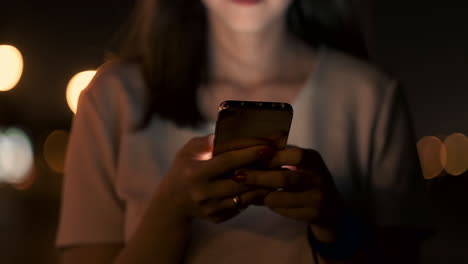 at night a young girl sits on the grass in a big city and looks into the smartphone screen writes a message and maintains her personal blog.