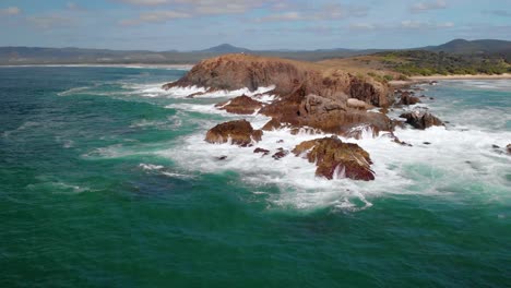 aerial view away from a rocky bay, at the emerald beach - reverse, drone shot