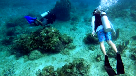 two scuba divers exploring ocean floor coral reef, fish swimming around, sand, rocks, oxygen tank making bubbles, wide shot, deep sea diving, cinematic