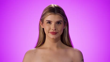 medium shot of a pretty young model taking off her visual aid or glasses and smiling happily and friendly into the camera in front of a purple background in slow motion