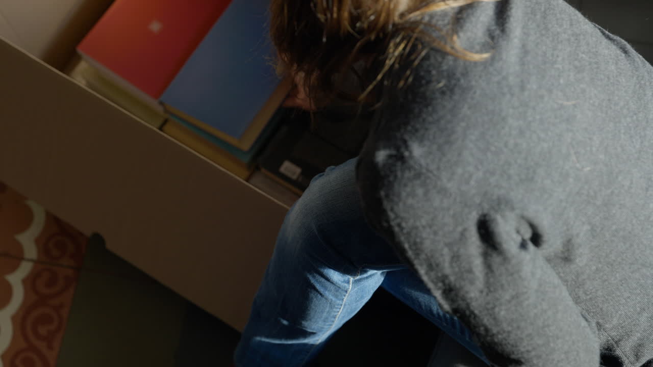 mujer sentada leyendo un libro y colocándola en una caja de cartón preparándose para la nueva reubicación de la casa