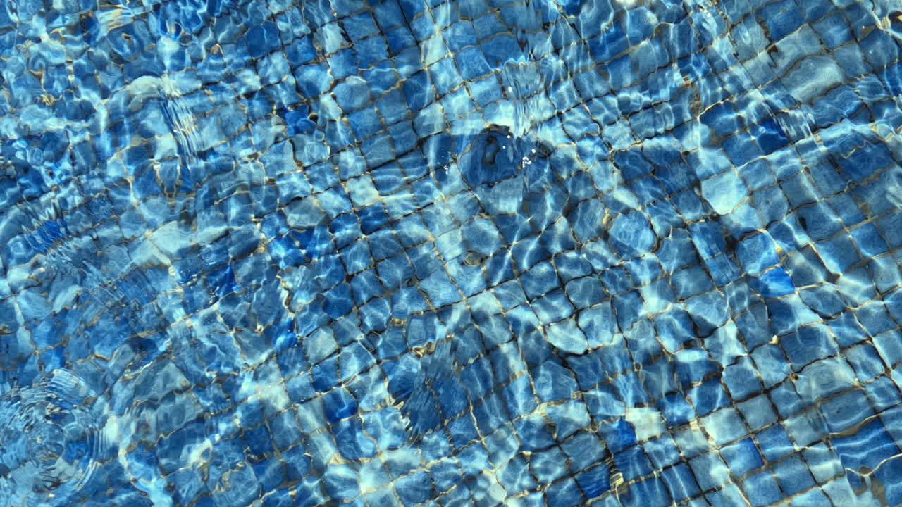 agua ondulada en la piscina azulejos azules y la luz del sol brillando