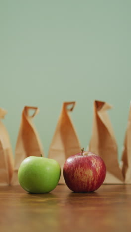 video vertical de manzana roja y verde con fila de almuerzos envasados en bolsas de papel y fondo gris