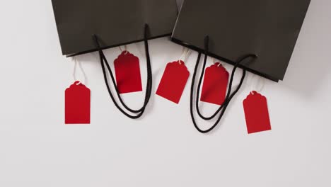 Two-black-gift-bags-with-five-red-sale-tags-on-white-background-with-copy-space