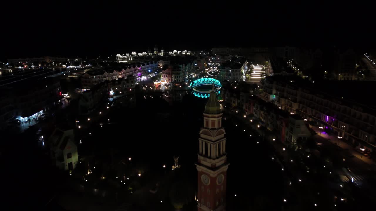 Close aerial shot of the Vietnamese night sky, the enchanting Grand World comes alive with vibrant illumination, trees lavishly adorned with a dazzling array of colorful lights. Clock tower.