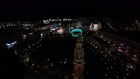 close aerial shot of the vietnamese night sky, the enchanting grand world comes alive with vibrant illumination, trees lavishly adorned with a dazzling array of colorful lights. clock tower.