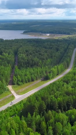 aerial view of a road winding through a lush green forest, with a lake in the background