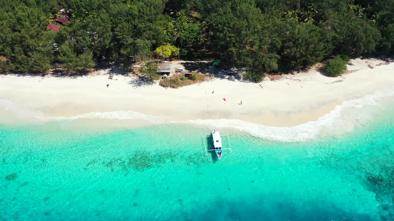 Traditional Asian boat anchoring on shore calm transparent water of azure lagoon washing white exotic beach of tropical island in Indonesia
