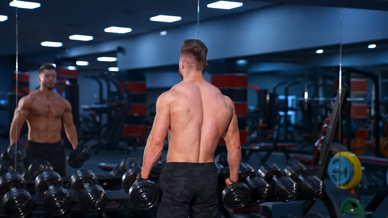 Strong young man with athletic body doing exercises with dumbbells. Fitness, bodybuilding. Health care. Slow motion.